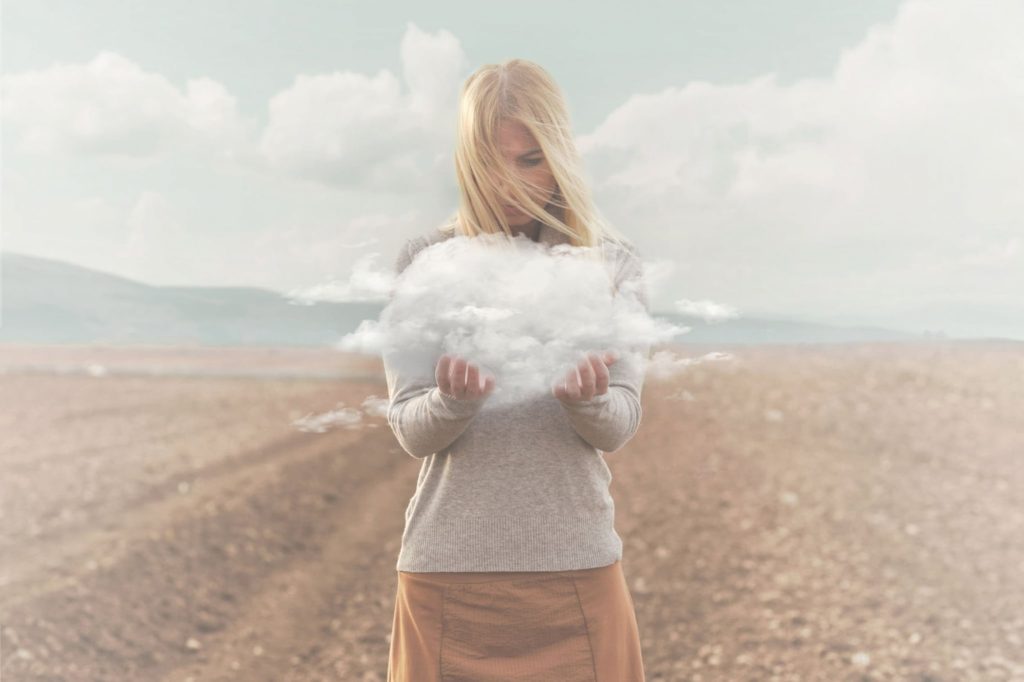 Woman standing in a field and holding a cloud in her hands