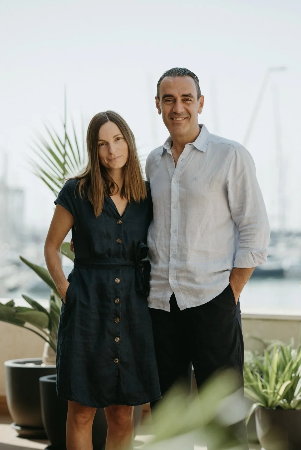 Two colleagues standing together on a terrace with potted plants, marina in the background