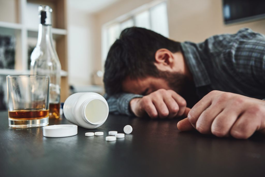 Dark-haired, man lying on the table, in the kitchen with pills spilled from a bottle