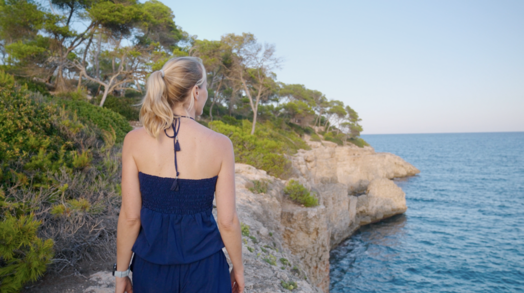 Woman standing on a rocky coastal cliff overlooking the sea and pine trees